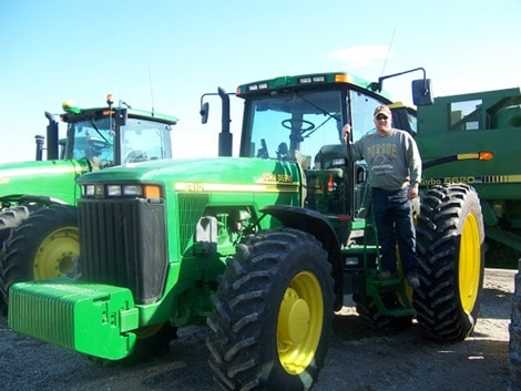 A farmer standing next to a green John Deere tractor.
