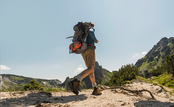 A person with a backpack hikes up a trail in a mountainous landscape under a clear sky, enjoying their first backpacking trip.