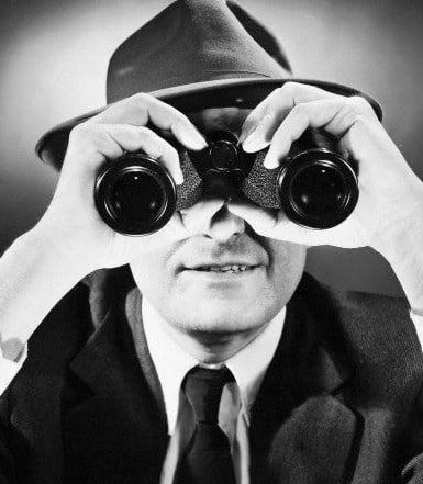 A man wearing a hat, going undercover and discreetly protecting his privacy online, intently looks through binoculars.