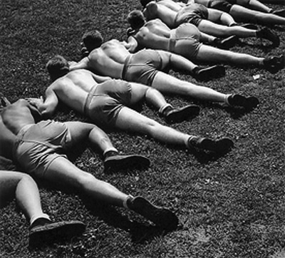 A black and white photo of a group of men doing WWII workouts on the ground.