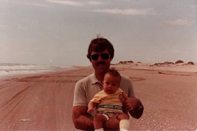 A man embracing life while tenderly holding a baby on a vibrant beach.