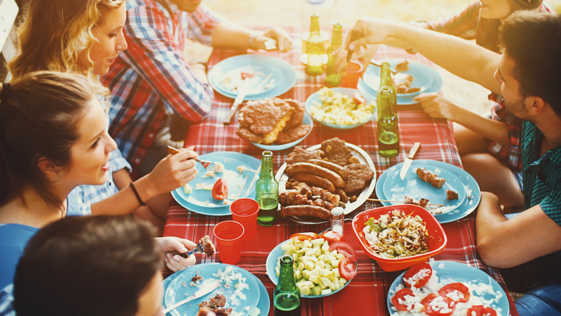 A group of people enjoying a weekend meal at a picnic table hosted by their friend.