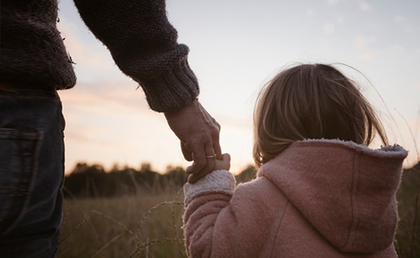 Father holding his daughter's hand outdoors at dusk, embodying the father-daughter relationship.