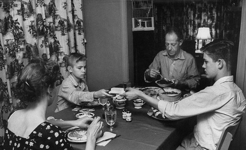 Vintage family eating at dinner table brother passing dish to brother.