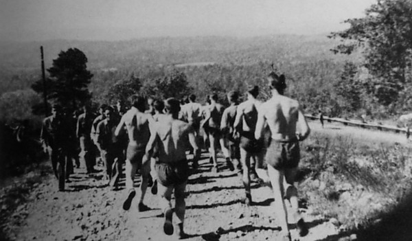 During WWII, a group of men is running on a dirt road as part of their workout regimen.