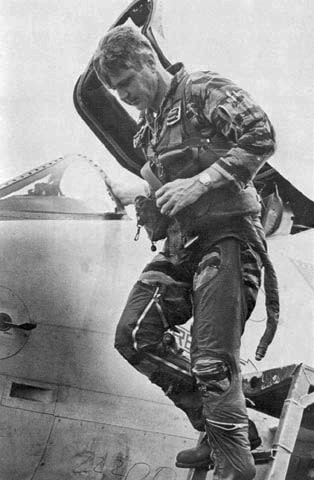 A military pilot in flight gear steps down from the cockpit of a jet aircraft, embodying resilience as he emerges with the open canopy behind him.