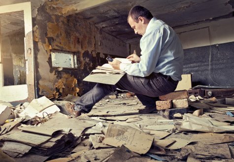 taxrecord Man sitting in dilapidated room surrounded by taxes papers.