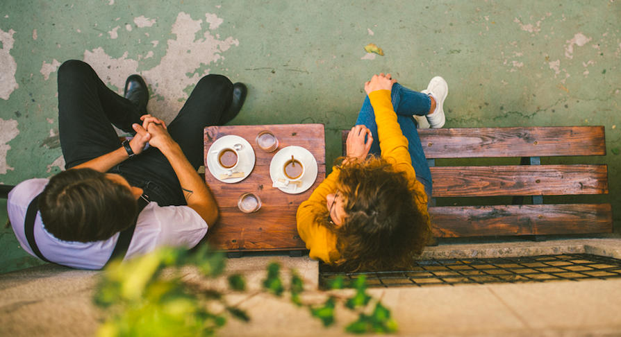 A man and woman sitting on a wooden bench, people enjoying each other's company.