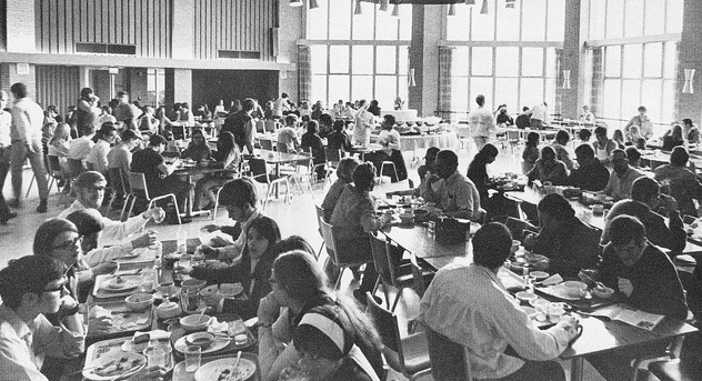 A black and white photo of people eating in a dining hall, showcasing college life.