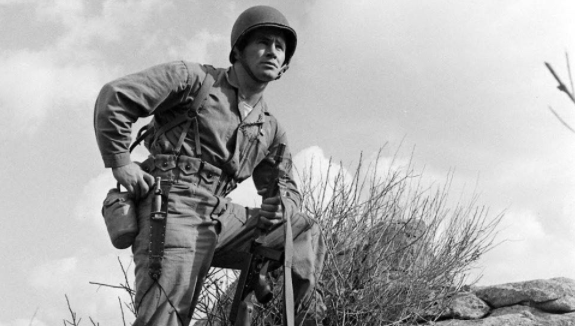 A Marine Corps soldier standing on top of a rock, showcasing his will to survive.