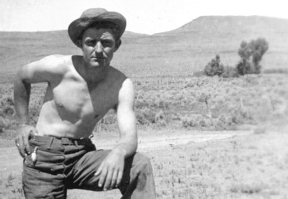 A tough man in a hat posing on a dirt road.